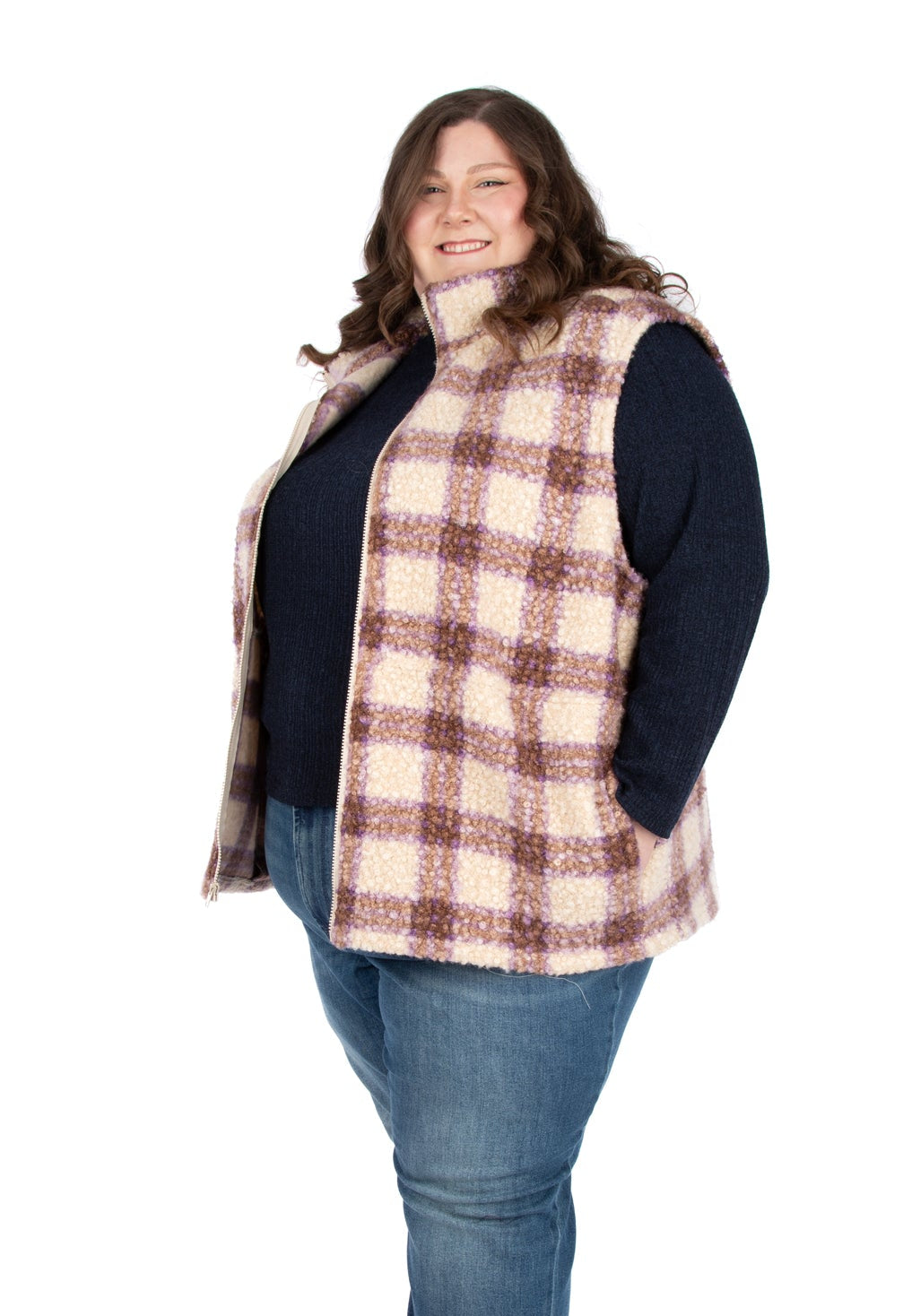 Woman wearing a plaid vest over a dark top and jeans on a white background