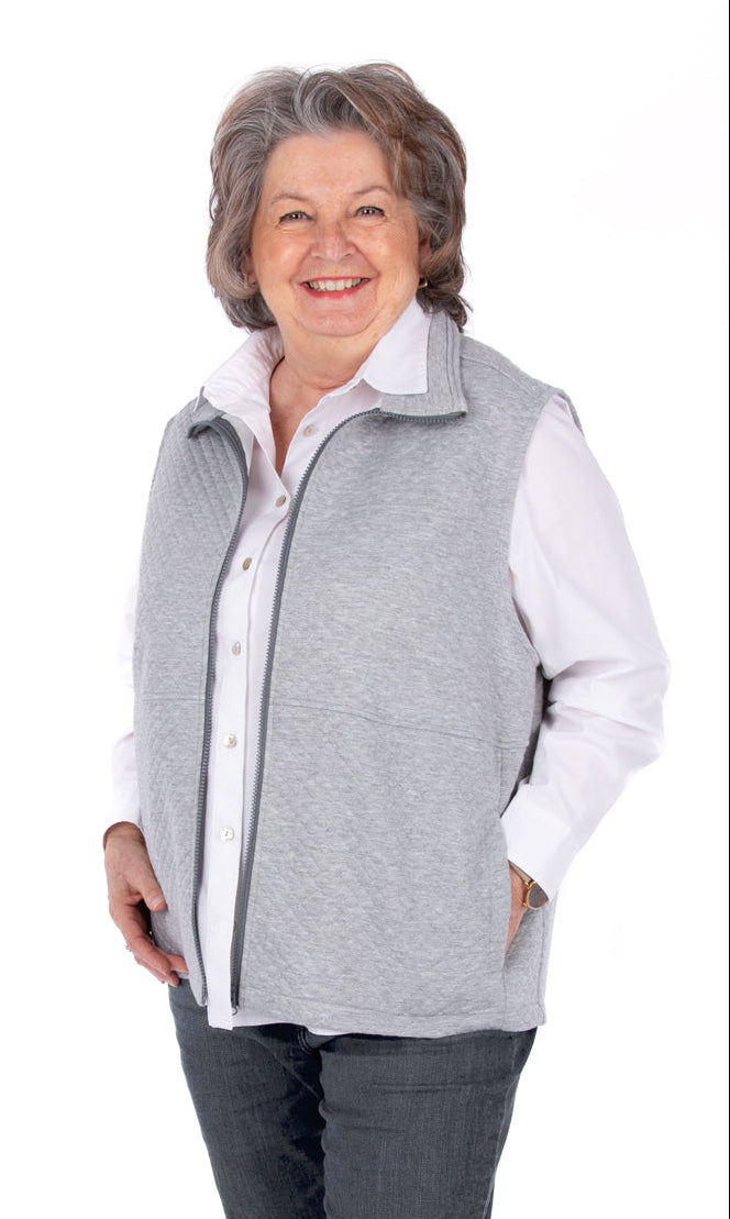 Woman wearing a gray vest over a white shirt with dark pants on a white background